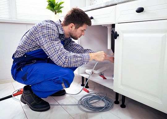 Instalator desfundând scurgerea cu spirala, sub chiuveta de bucătărie