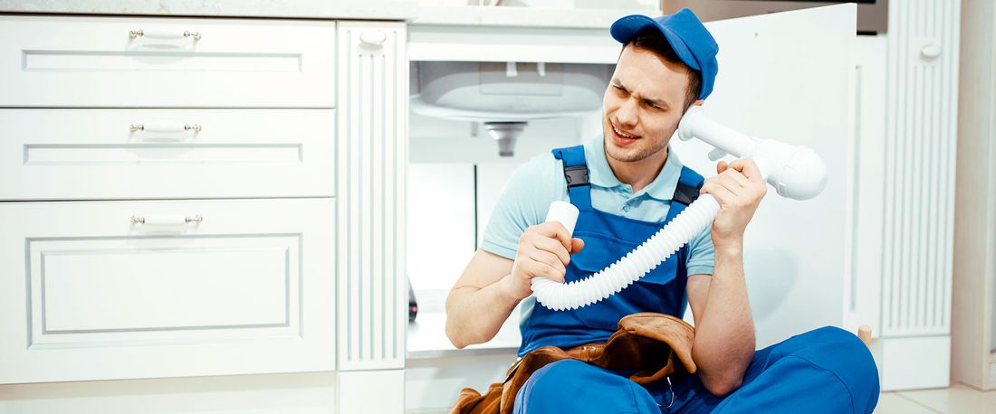 Instalator cu o țeavă PPR în mână, sub chiuveta din bucătărie
