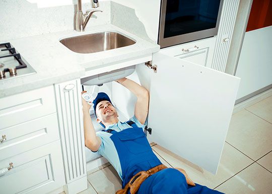 Instalator întins sub chiuveta dintr-o bucătărie albă